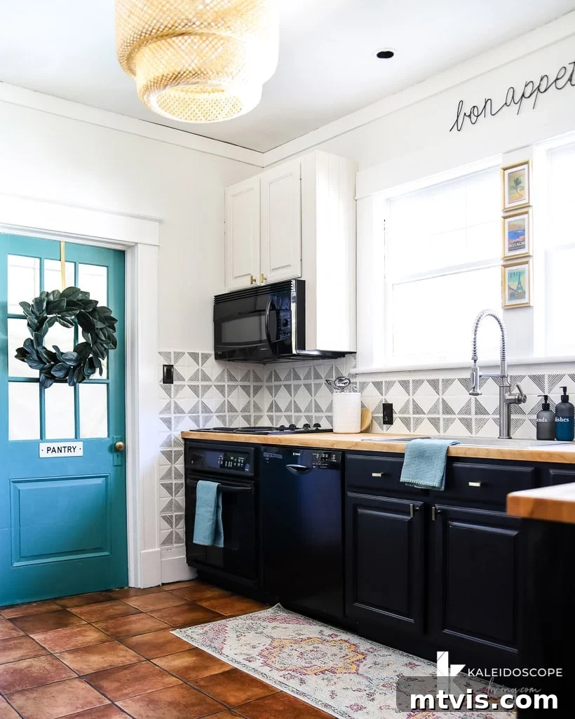 DIY Kitchen Transformation Under One Thousand 14 A kitchen corner with a blue door with a wreath and a sign that says "pantry," partial tiled walls, white upper cabinets and blackish lower cabinets.