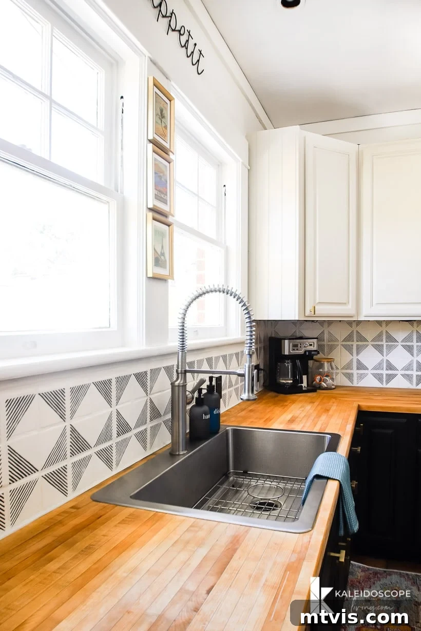 DIY Kitchen Transformation Under One Thousand 16 A black and white budget-friendly kitchen makeover has geometric black and white tiles as a backsplash, a treated wood countertop, stainless steel sink, two large windows and white cabinets. A coffee machine in the corner.