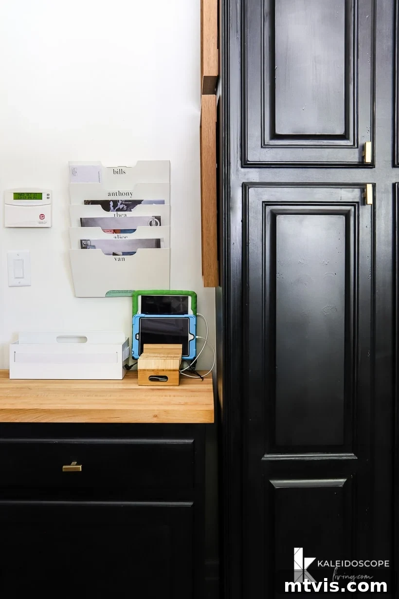DIY Kitchen Transformation Under One Thousand 17 Part of a pantry door painted black, next to a wood countertop family command center with wall-mounted file trays with family member's names and a charging station for children's tablets.
