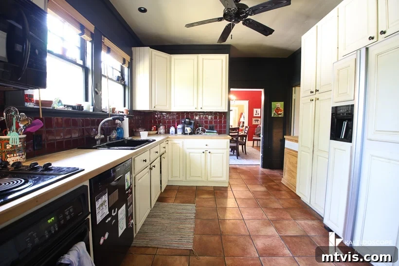 DIY Kitchen Transformation Under One Thousand 4 A view into a large but narrow outdated kitchen before budget-friendly kitchen makeover. The left side holds the counter, stove, oven, sink and cabinets and the right side has a white refrigerator, pantry and upper cabinets.