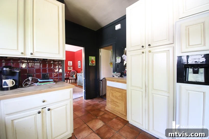 DIY Kitchen Transformation Under One Thousand 5 A different view of the back half of an outdated kitchen before budget-friendly kitchen makeover shows white cabinets, dark walls, and a narrow entry.