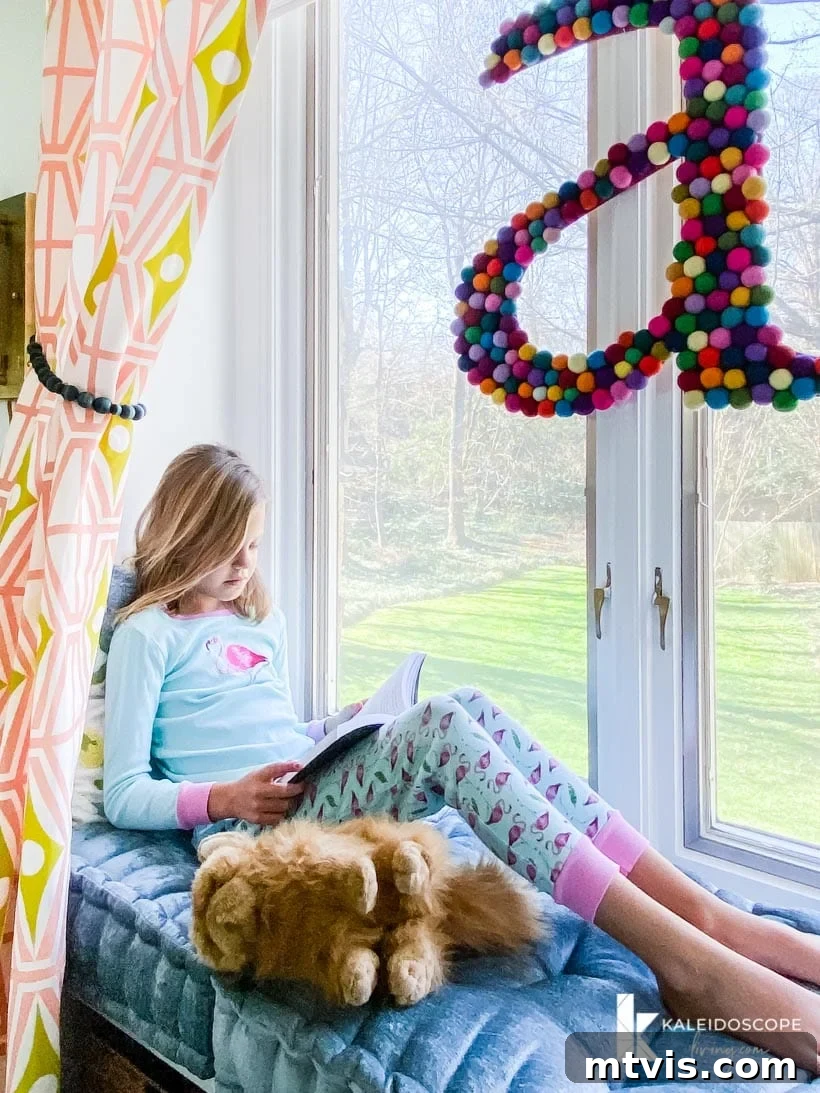 Close-up of the charming window seat in Attley's colorful girl's room, showcasing fluffy pillows, decorative cushions, and vibrant patterned curtains from Spoonflower, perfect for a cozy reading nook.