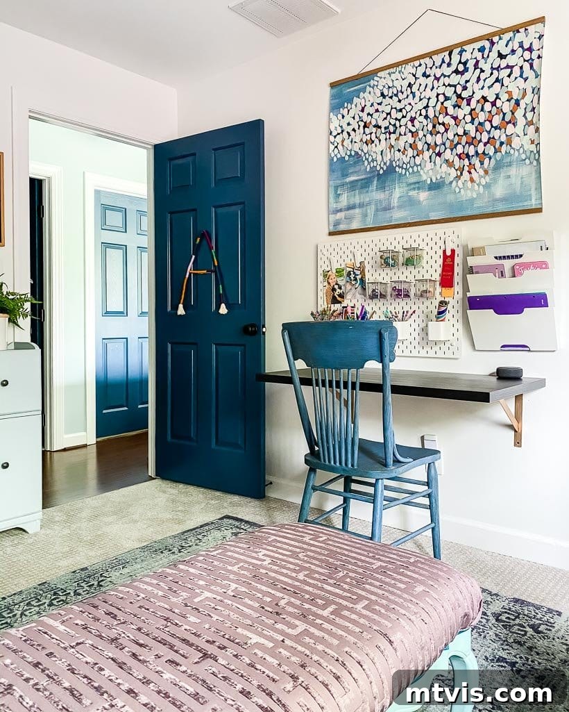 The Big Reveal: Avery's Bespoke Bunk Bed Room 12 A young girl's bedroom door is painted blue to match the chair in front of a wall-mounted desk, pegboard and large art piece.