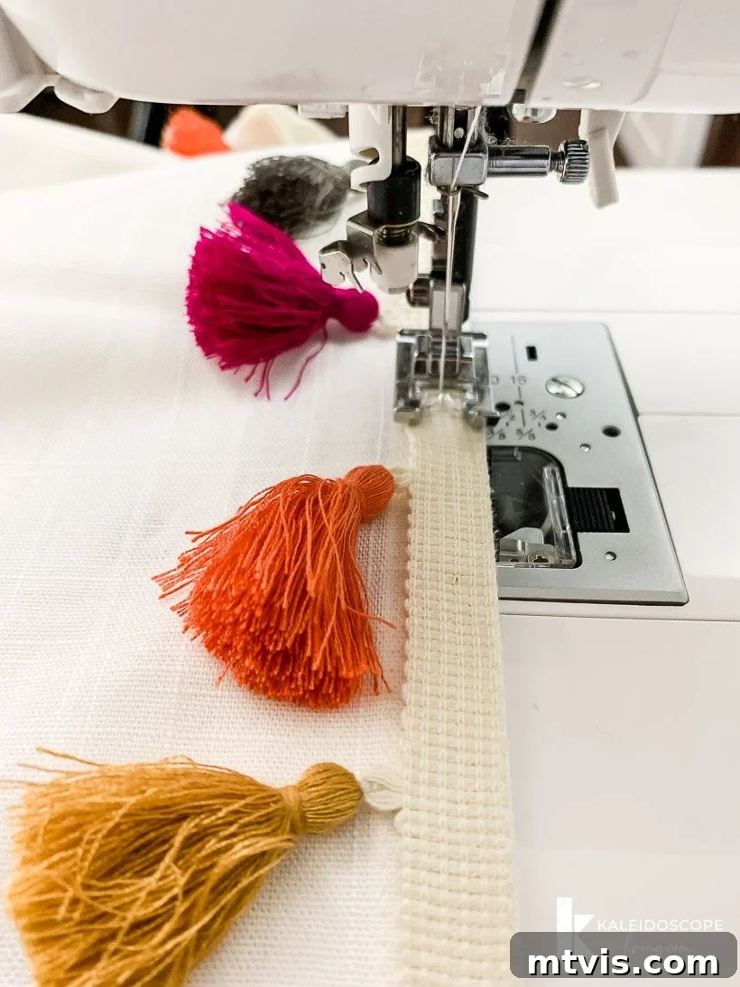 A sewing machine expertly stitching colorful tassel trim along the edge of a curtain panel, illustrating the final attachment process.