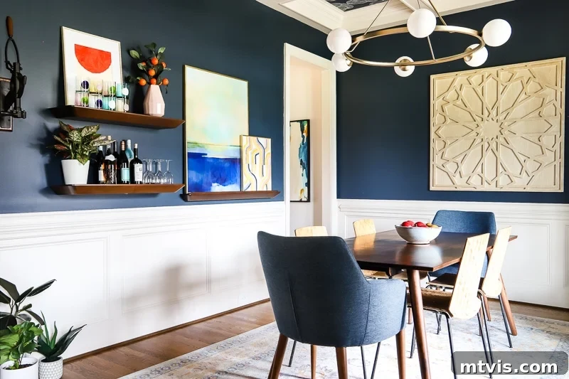Step Inside Our Navy Blue Dining Room 6 A navy-blue dining room reveal is complete, featuring classic white wainscoting, an elegant round light fixture, a charming small dining room table, and captivating wall art, creating a sophisticated and inviting space.