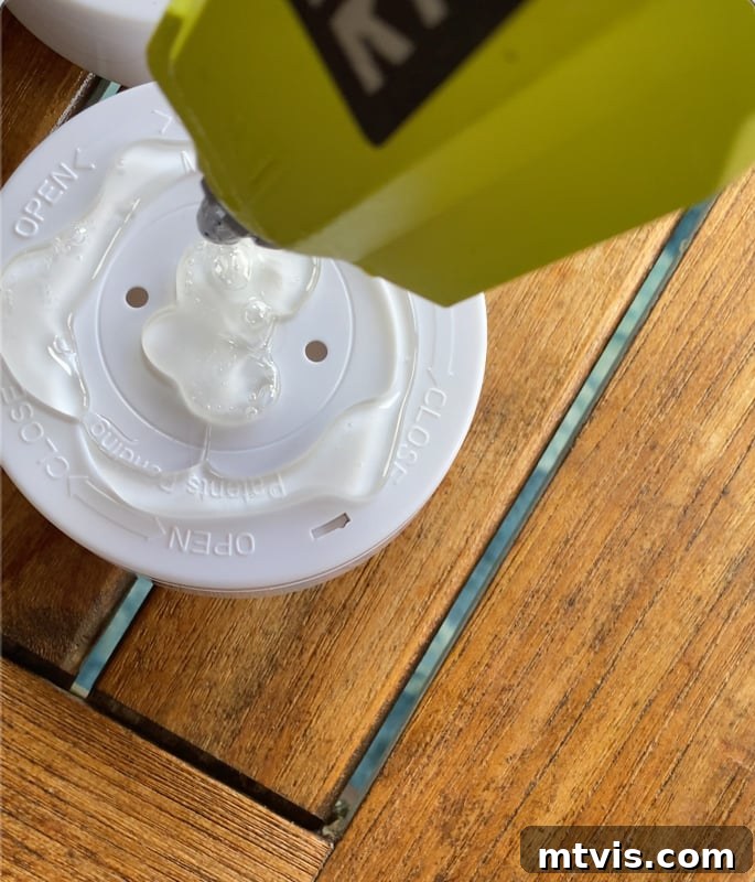 Build Your Own Outdoor Chandelier 11 Applying hot glue to the back of a puck light before attaching it inside the basket shade of the DIY outdoor chandelier.