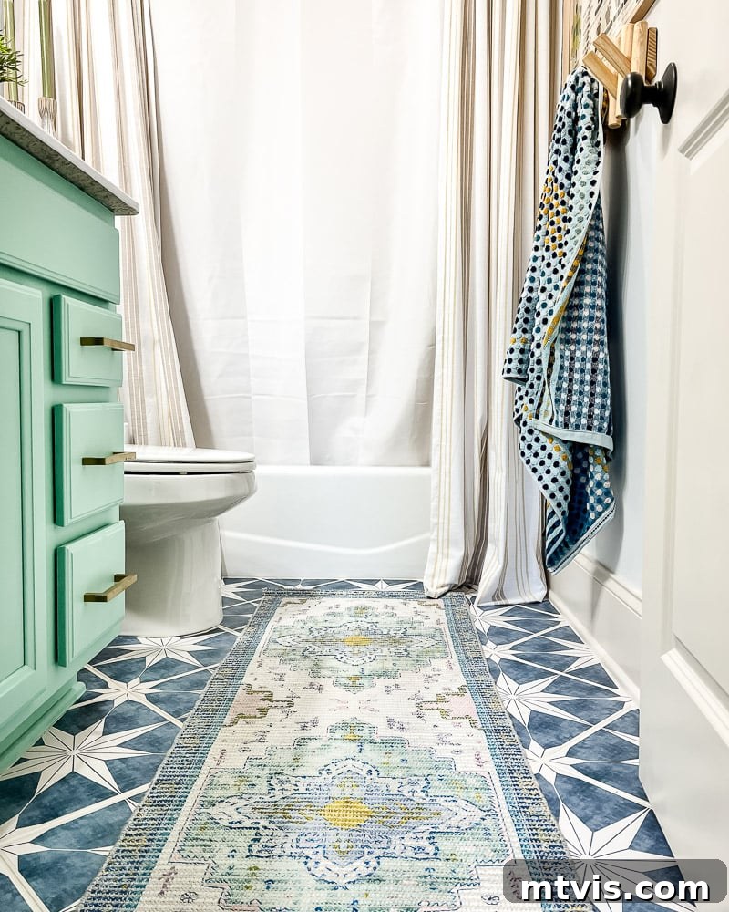Splash of Style: Top Bath Mats for Bright Bathrooms 3 A beautifully designed bathroom features a mint green sink cabinet and an eye-catching blue overdyed vintage bath mat runner laid across blue-starred tiles, extending from the door to the bathtub. A towel rack is visible on the right wall, showcasing how a bath mat can be a crucial design element.