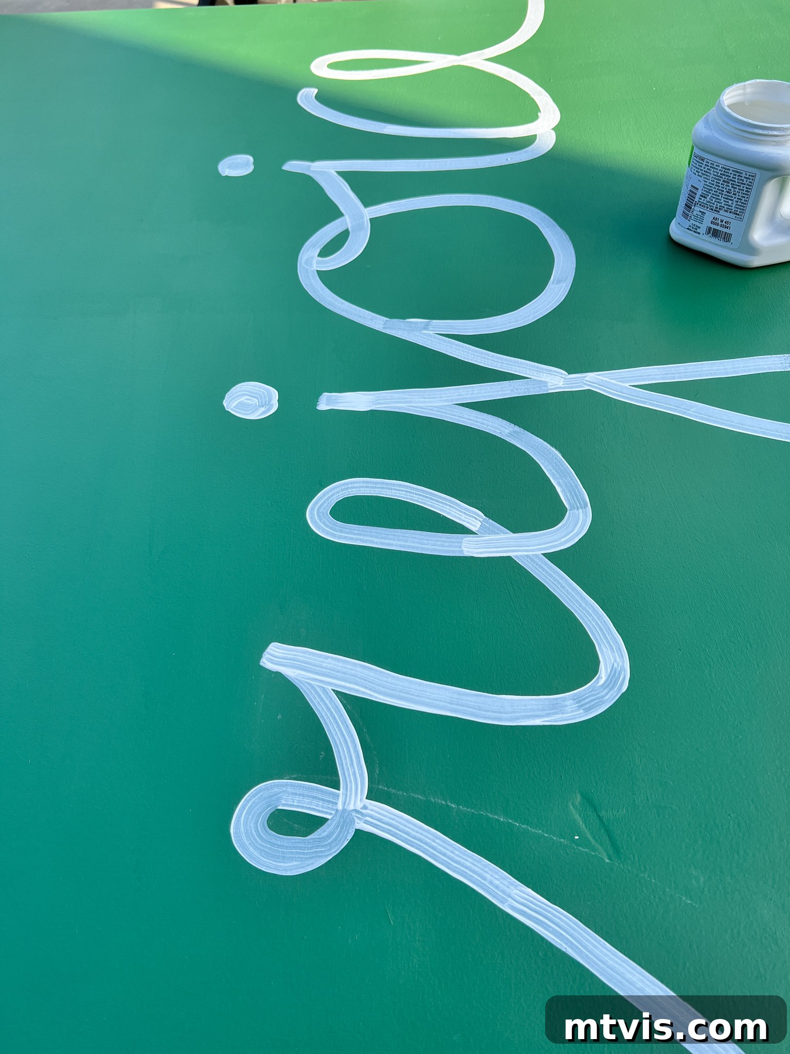 First coat of white paint applied to the 'Rejoice' design on green plywood