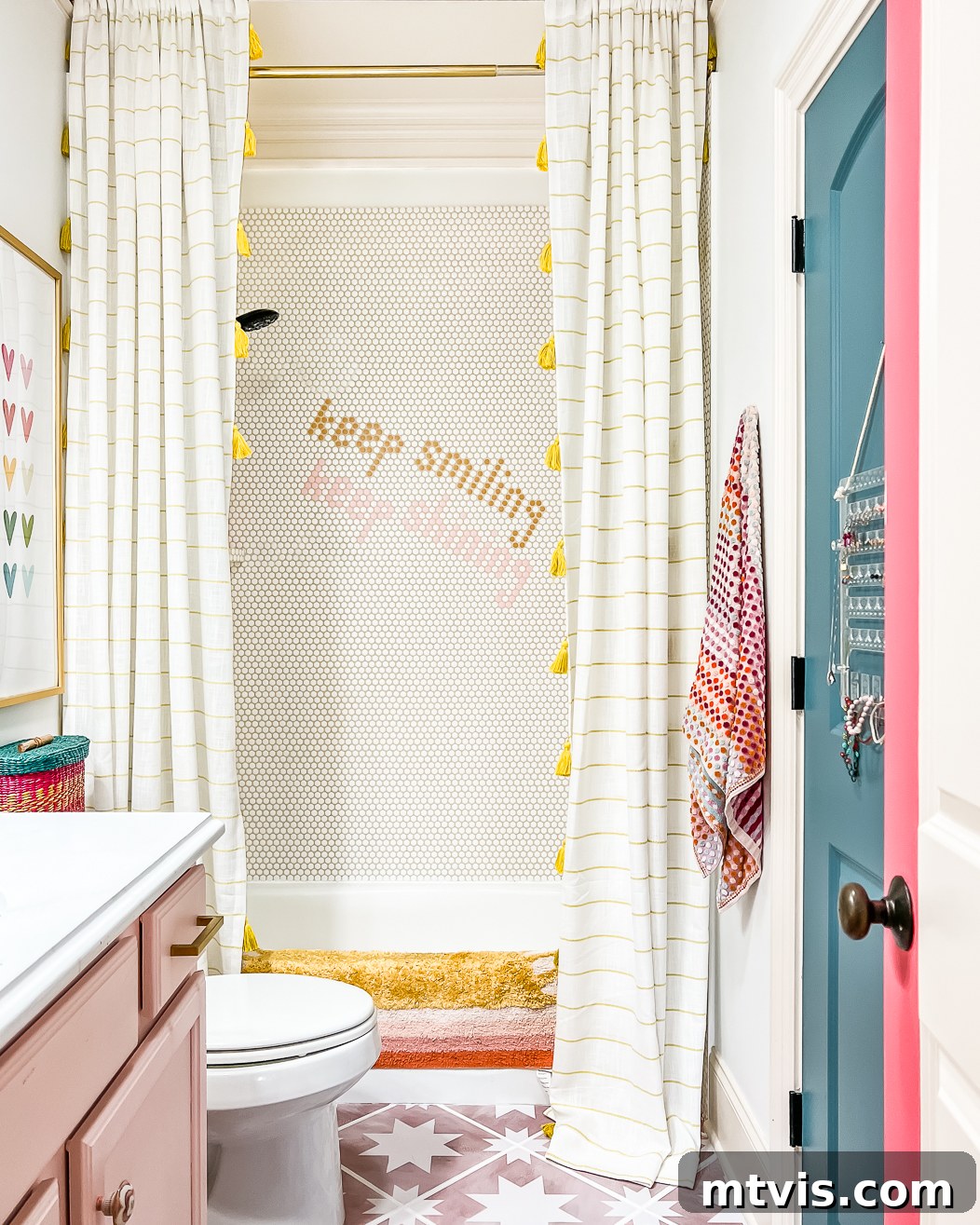 A bright white and pink girl's bathroom after an affordable renovation has a pink cabinet, and floor to ceiling curtains over the shower. 