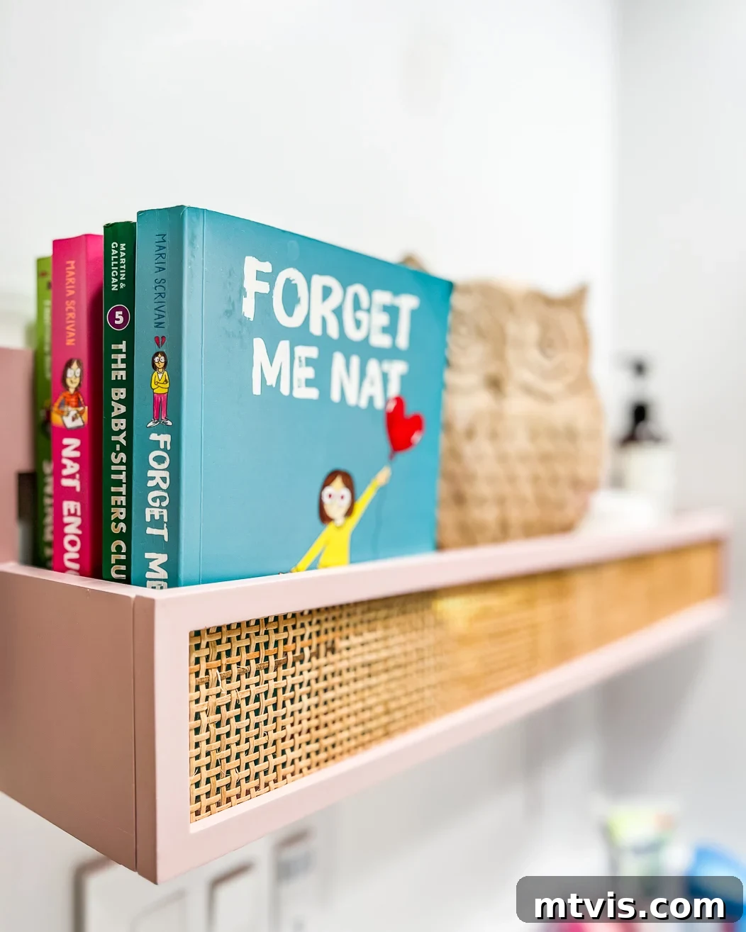 A close-up of a muted pink and caned hanging wall box full of books, and owl statue, and lotions. 