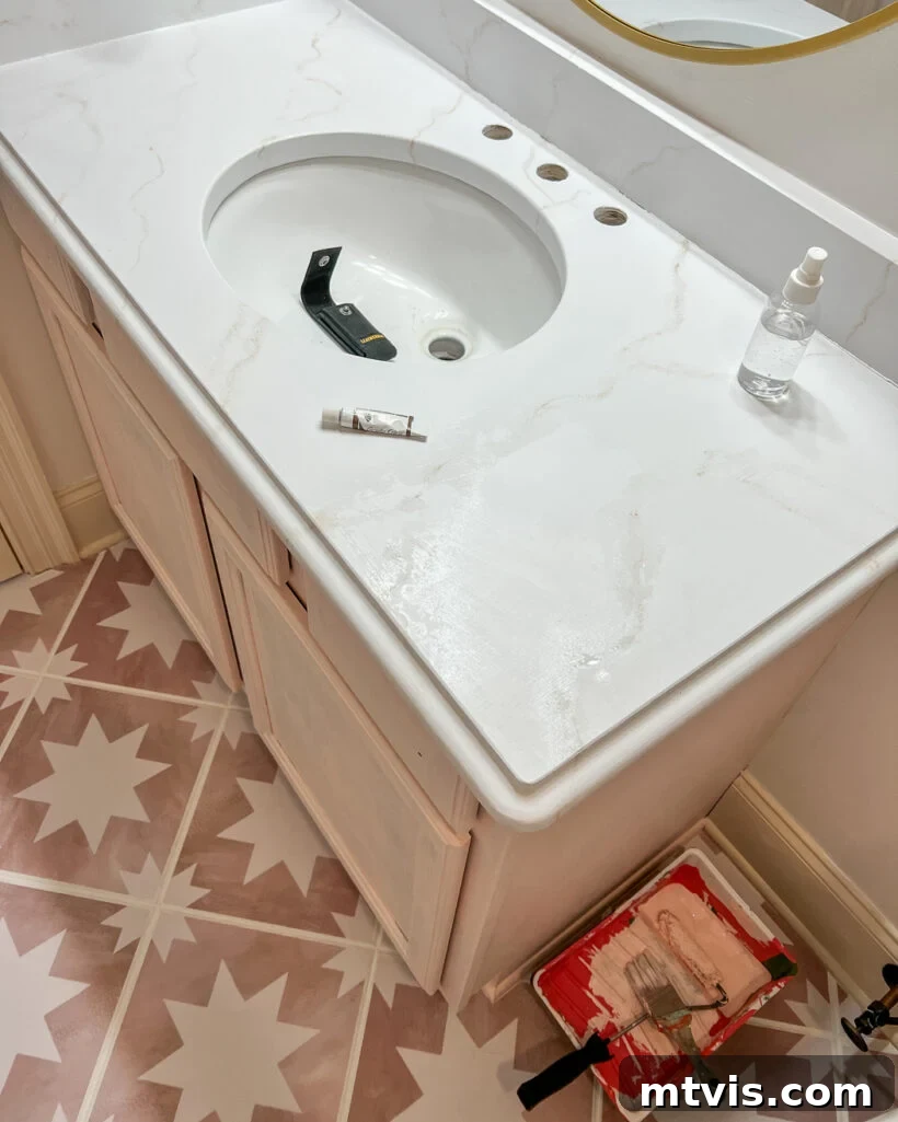 An overhead view of a bathroom countertop painted to look like white marble, with a light pink under-cabinet and geometric flooring. 