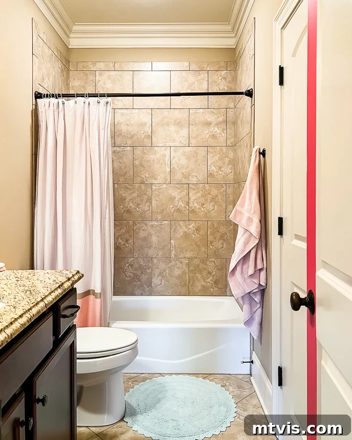 A "before" photo of a brown and tan outdated bathroom with a tub, shower, toilet, and sink cabinet. 