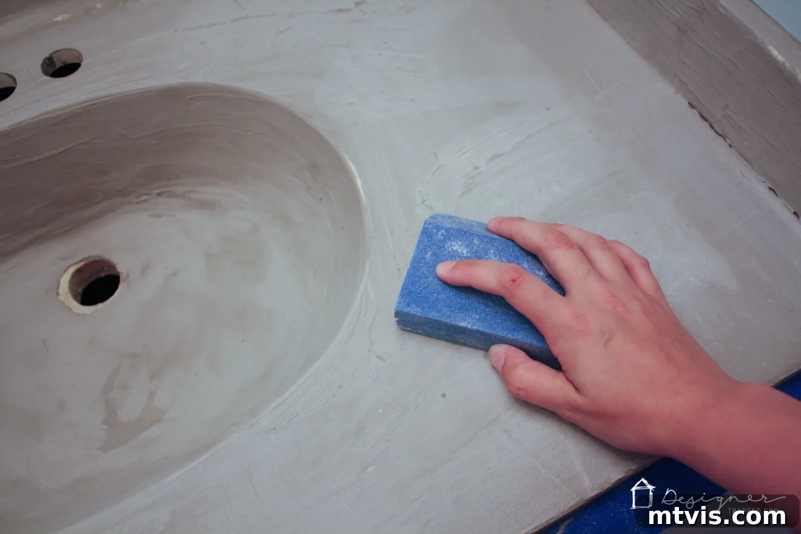Effortless DIY Concrete Vanity and Sink No Forms No Heavy Lifting 7 A person lightly hand-sanding the first dried coat of concrete overlay on a bathroom vanity, preparing the surface for subsequent layers.