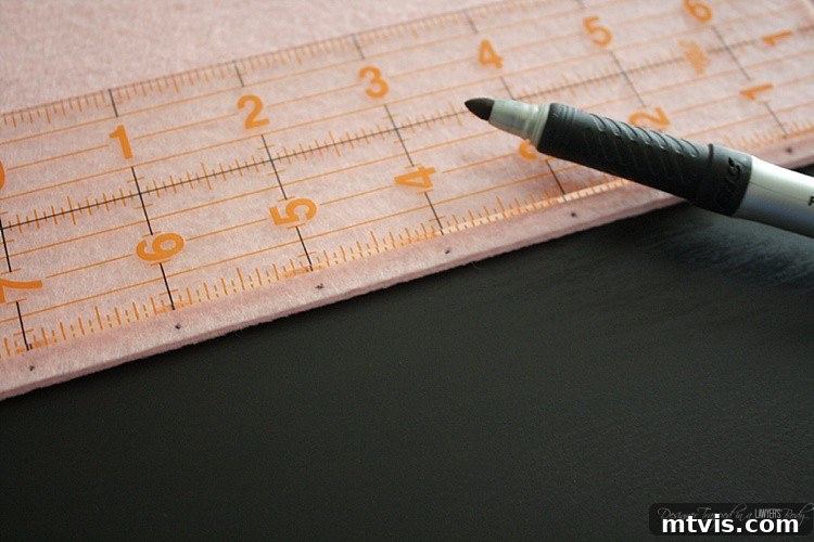 Felt Doll Magic: Create Your Own Playtime Friends 7 A ruler and marker are used to measure and mark 1-inch increments along the edge of a stiff felt piece, preparing it for hole punching.