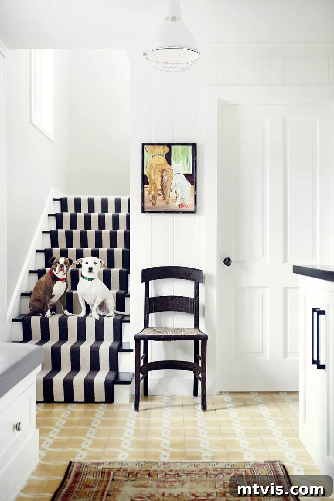 Elevate Your Entryway: Creative Stair Runner Designs 18 An indoor-outdoor black and white striped carpet runner adorning stairs, currently occupied by two dogs. A black accent chair and crisp white walls and cabinets are visible to the right, completing a chic and pet-friendly interior.