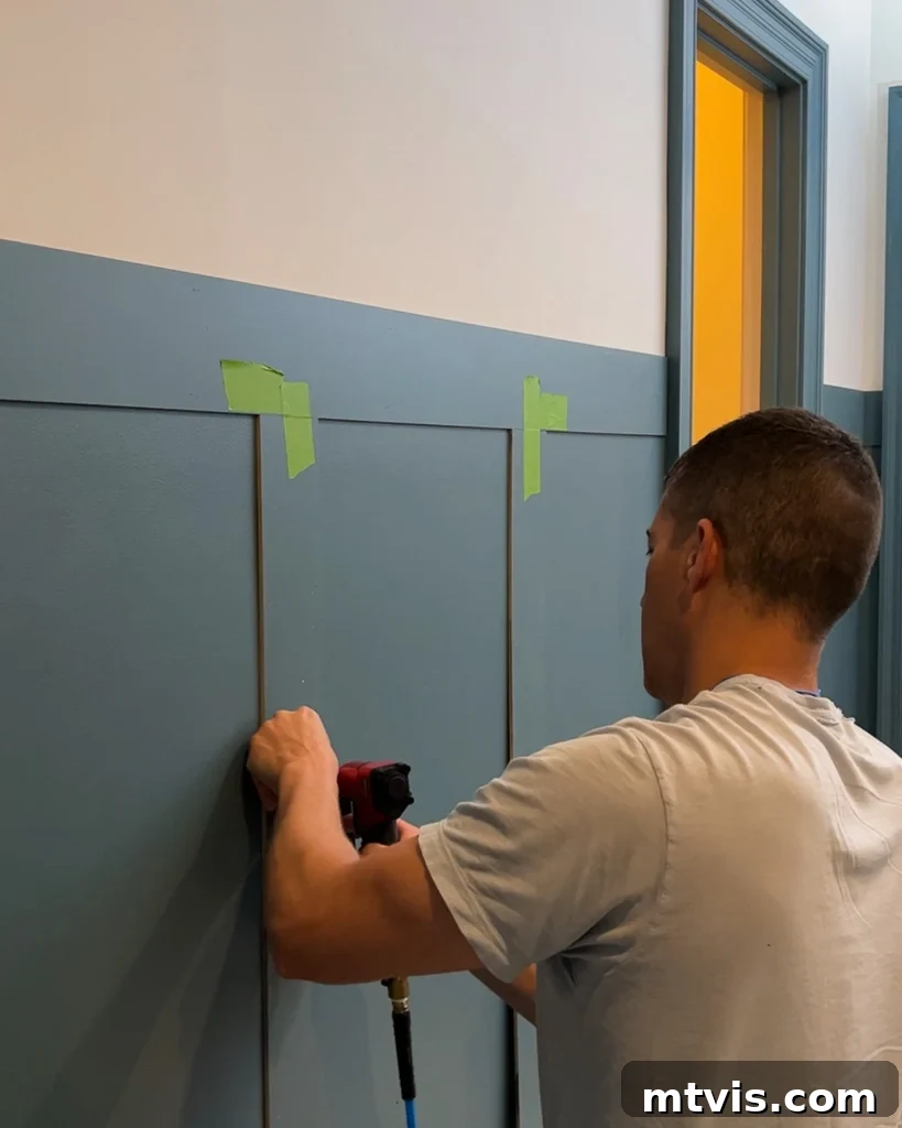 Effortless Board and Batten Accent Wall DIY 9 Attaching vertical battens to the wall with a pin nailer, ensuring they are level