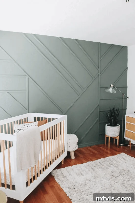 A nursery is shown with a sage grey accent wall that features interesting geometric board and batten patterns. 