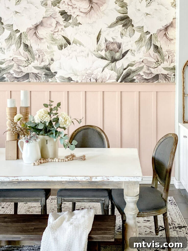 A dining table is showcased in front of a soft pink board and batten wall and large floral wallpaper. 