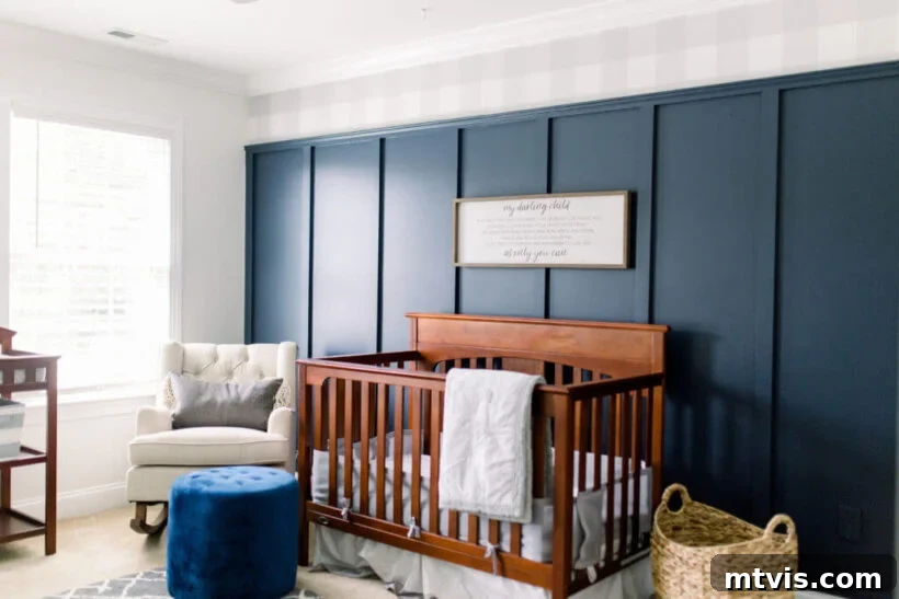 A baby’s room with a dark wood crib features an eye-catching navy blue board and batten wall with buffalo plaid wallpaper on top.