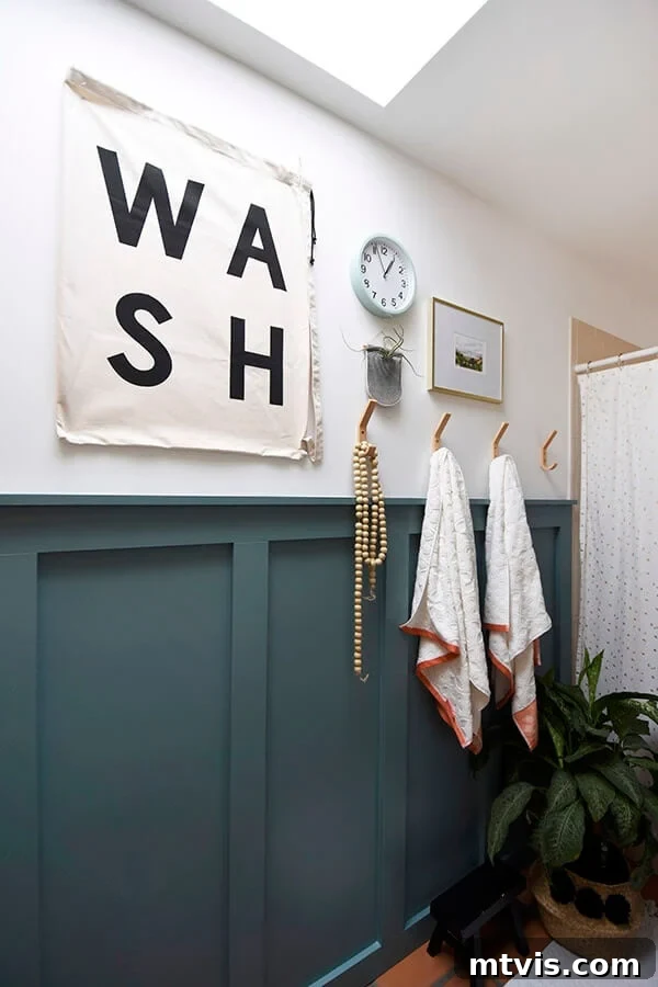 A bathroom has a modern twist with dark teal board and batten to complement graphic art and gold towel hooks. 