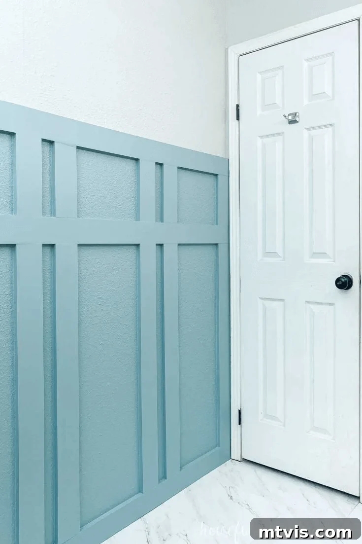 A blue board and batten bathroom wall is shown against white accents, a door, and flooring; the accent wall features unique batten spacing.