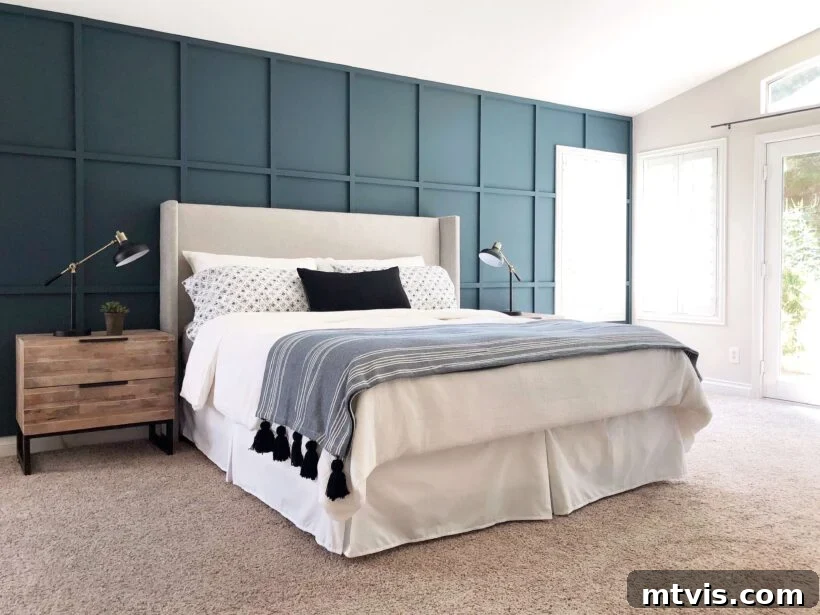 A double bed is shown with white linens and a dark blue accent pillow; the bed is in front of a deep turquoise accent wall with board and batten grid design. 