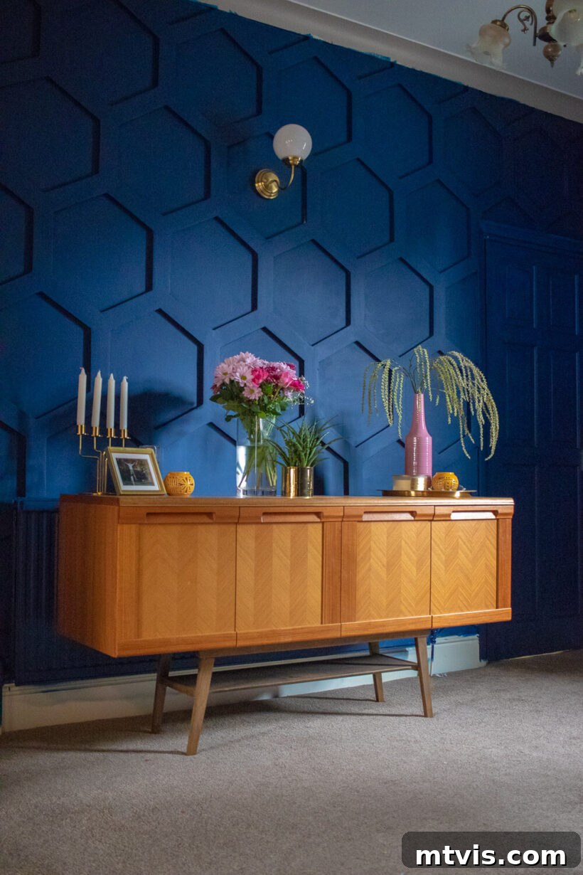 Board and batten walls are designed in a hexagon shape to create an interesting deep blue wall behind a mid-century modern sideboard with décor. 