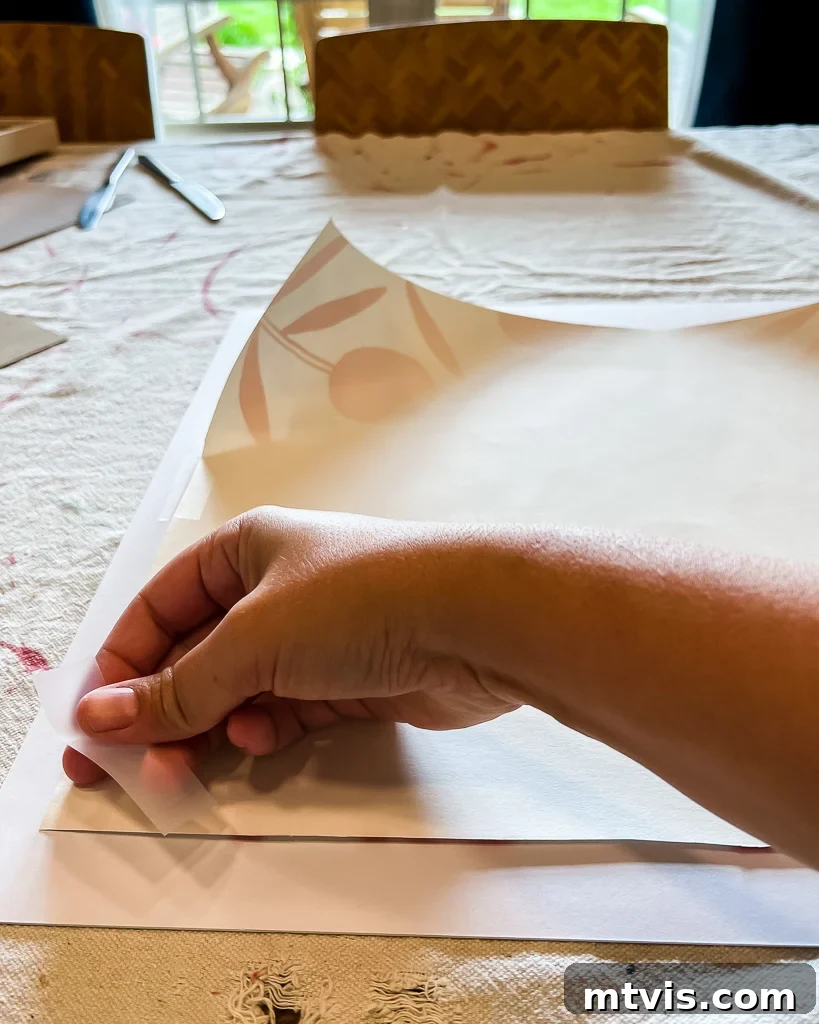 Hands taping a piece of patterned wallpaper to the back of a white photo mat, preparing it for framing.