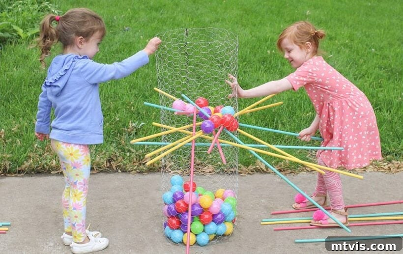 A colorful Ker-Plunk game is set up in a grassy yard and played by two children; the colorful balls are in a wire net, and the pins are in place. 