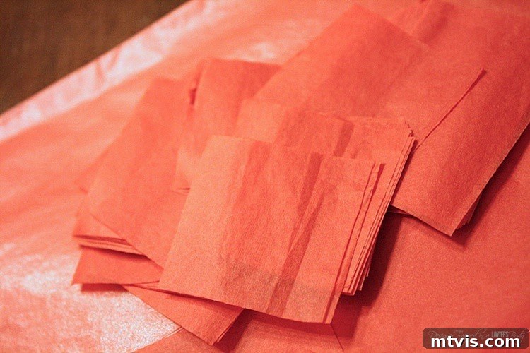 Valentines Door Decor DIY 11 A stack of red tissue paper being cut into 1-inch squares with scissors.