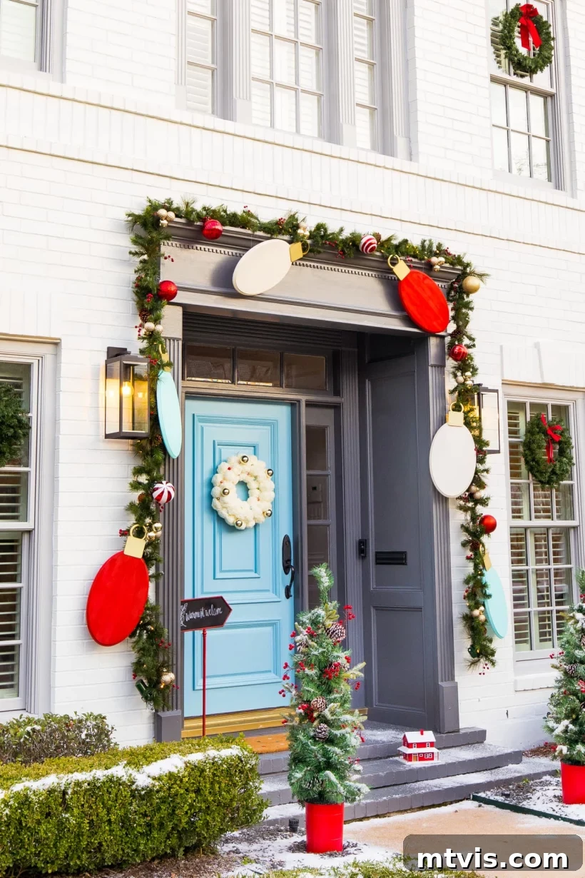 Festive Front Porch Christmas Magic 9 Front porch Christmas decorations by Sugar and Cloth include oversized light bulb cutouts in red, white, and teal hanging from garland that frames the entry. A bright turquoise front door features a fluffy white wreath. Two mini-Christmas trees in red pots are on either side of the steps.