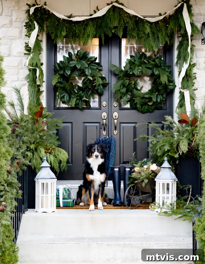 Festive Front Porch Christmas Magic 11 Craftberry Bush front porch Christmas decorations use greenery to create a festive atmosphere, like bushy garlands around the entry, large wreaths on the doors, and mini evergreen trees on either side of the dog sitting on the top step.