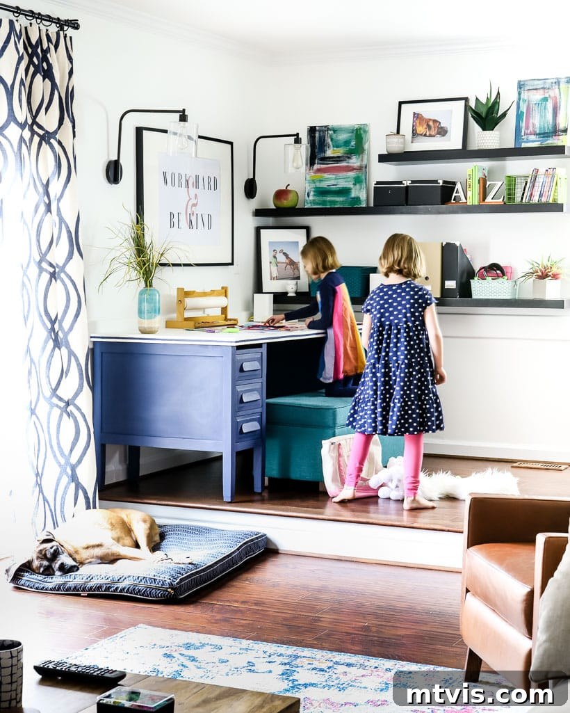 Playful and Chic Playroom Design Guide 9 A playroom in the corner of family room, including a desk, and two young girls near low bookshelves. Room by Tasha Agruso of Kaleidoscope Living
