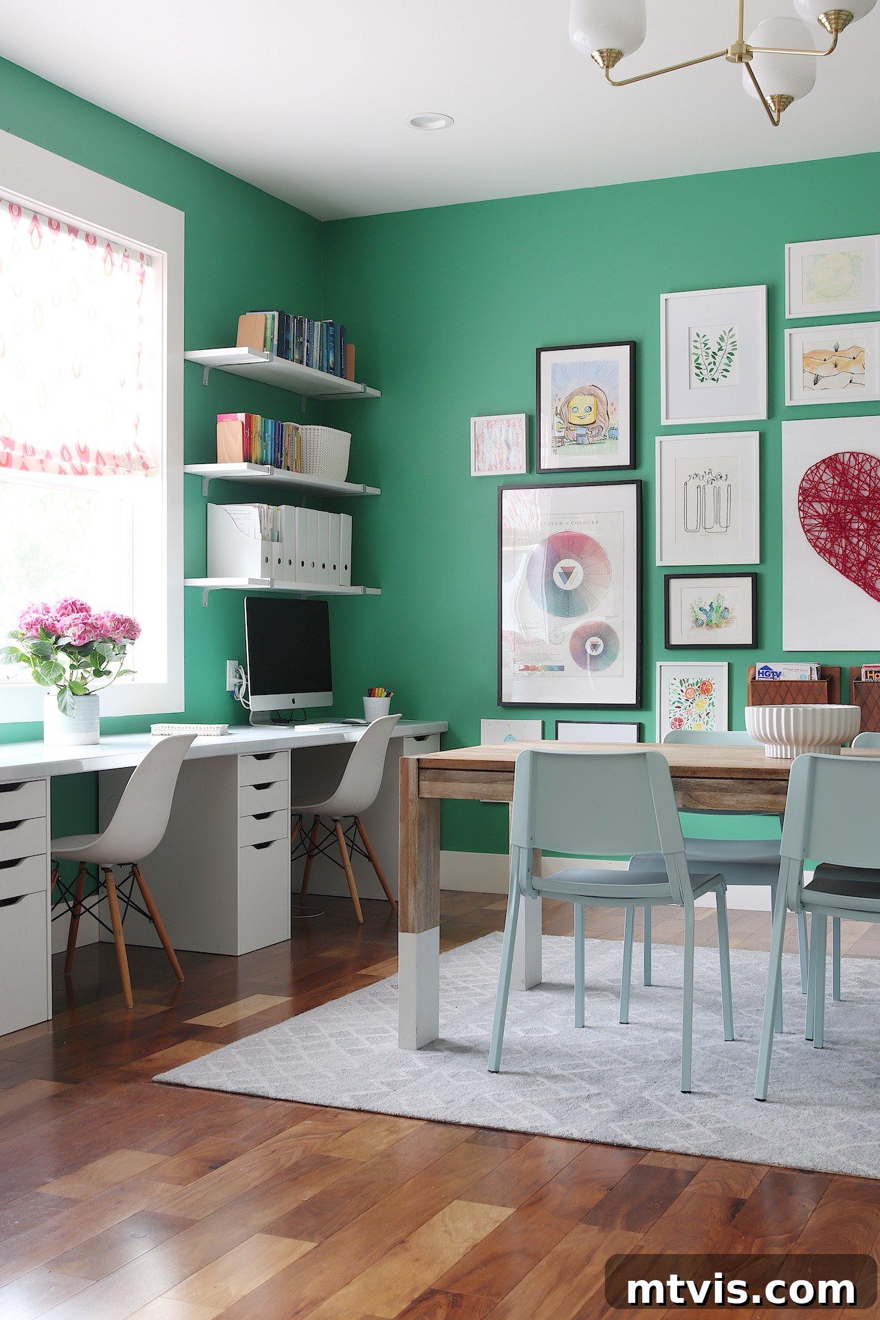 Playful and Chic Playroom Design Guide 17 A green room has white desks for homework against the windows and a craft table in the middle of the room/ Th walls are covered in framed pictures and art, which is just one of many playroom ideas.