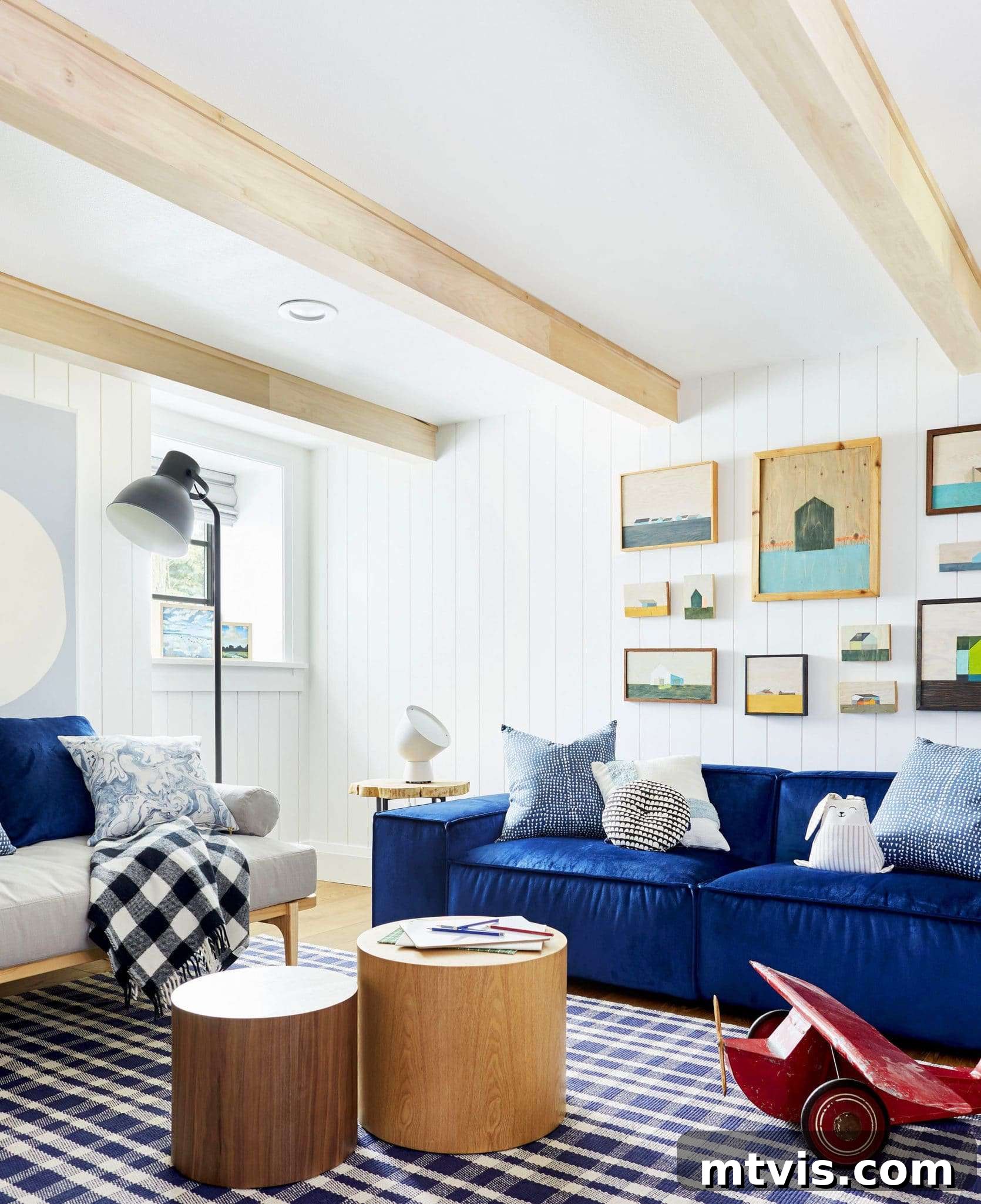 Playful and Chic Playroom Design Guide 20 Light wood beams make an interesting ceiling for a white wood paneled room with deep blue couches. A grey futon, round wood coffee tables and part of a large wooden toy plane complete this playroom idea.