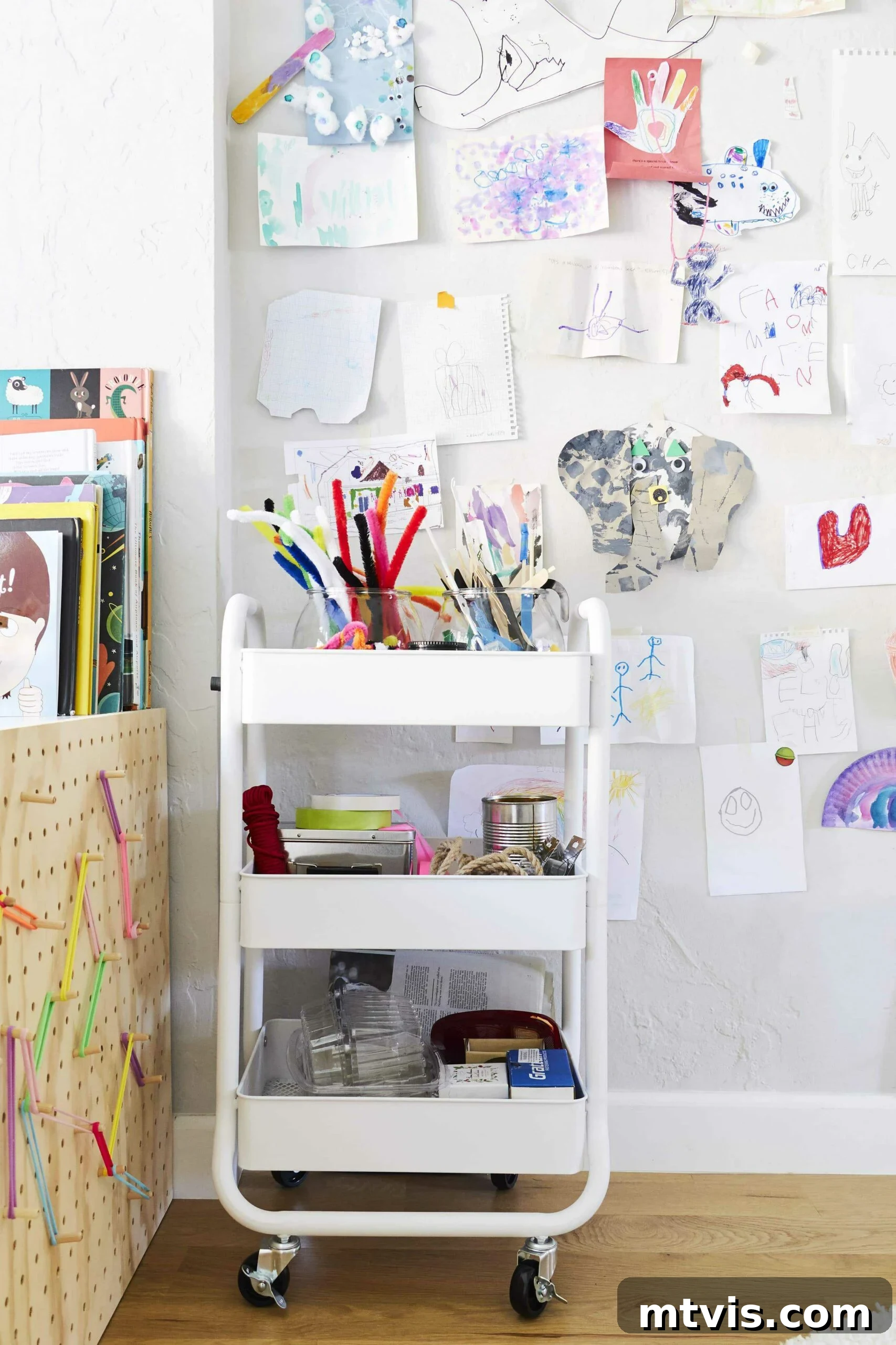 Playful and Chic Playroom Design Guide 27 One of the best playroom ideas is to use children's artwork as decoration. A wall of kid's art includes an elephant, handprints, and more crafts. Books and an art cart are in front.