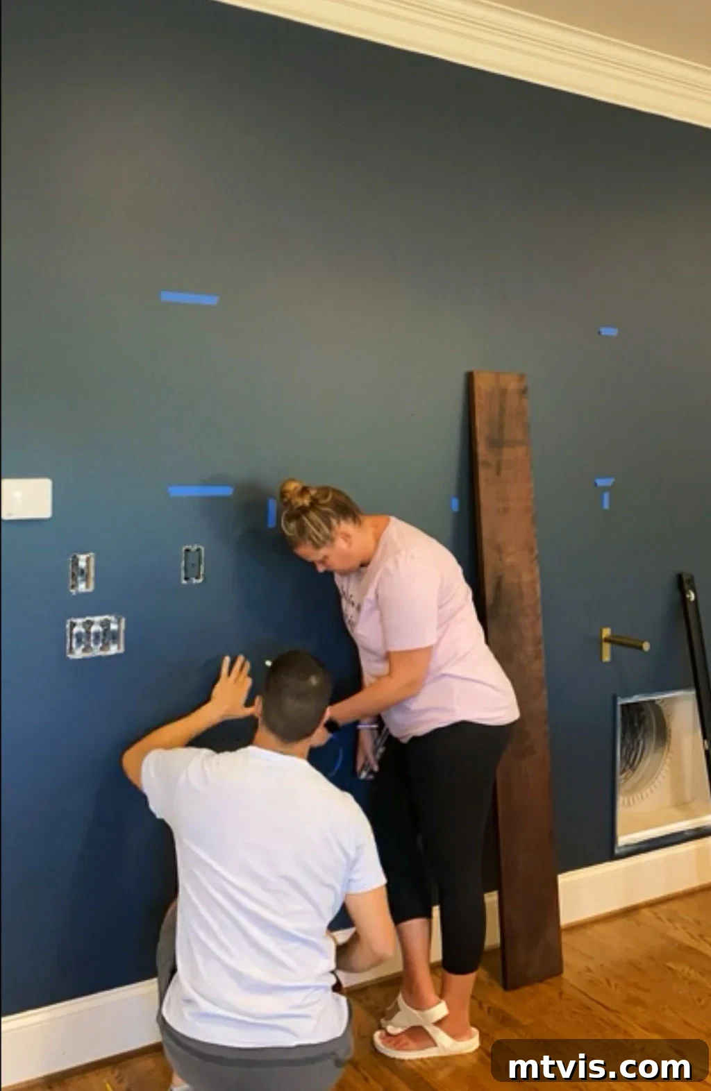 A person installing a metal shelf bracket onto a wall, aligning it with a marked stud location.