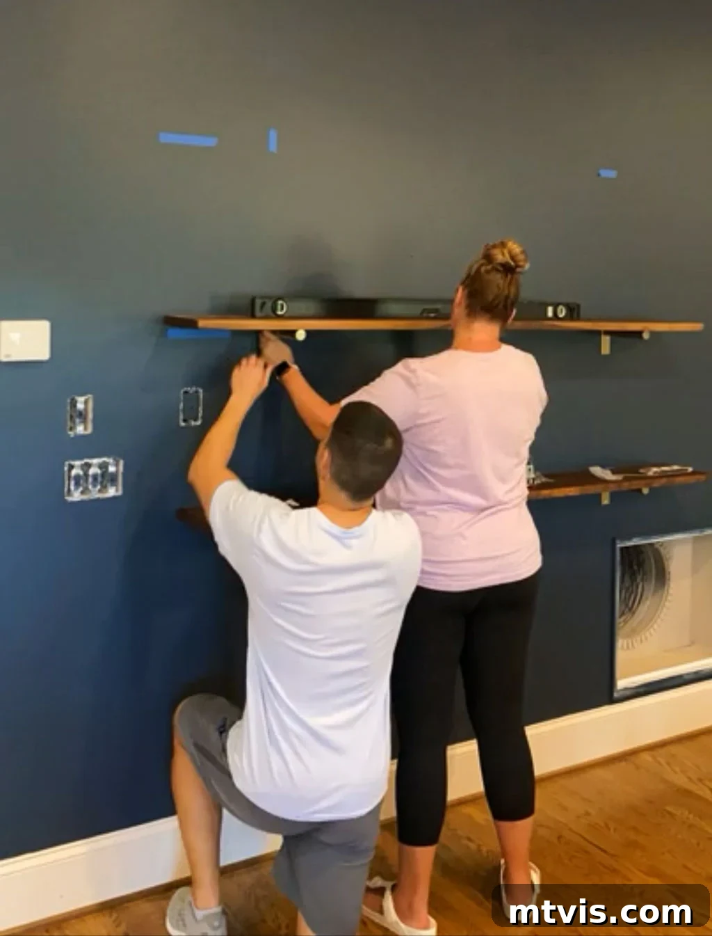 A person carefully placing a finished wooden shelf onto installed metal brackets, preparing to secure it.