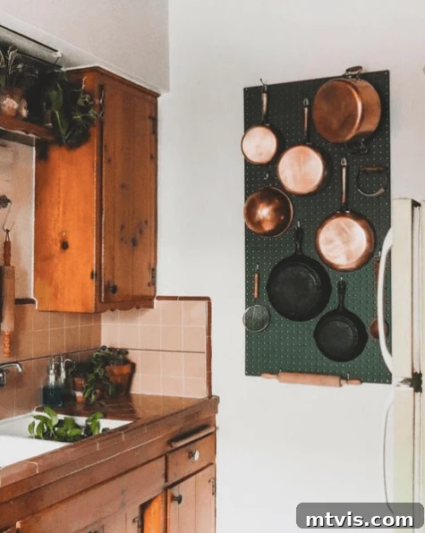 Dark green pegboard displaying copper and cast iron pots and pans in a stylish kitchen