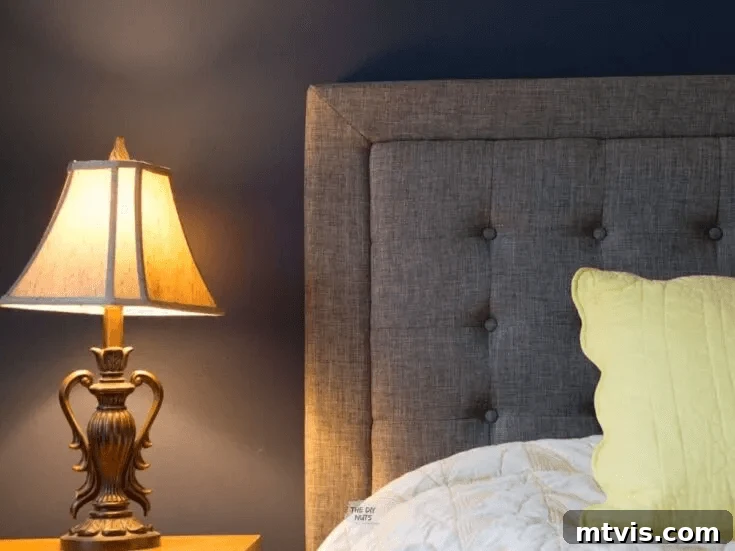 Sophisticated Serenity: Top Blue-Gray Paint Colors 9 A closeup of a bedside lamp and navy bedroom wall with upholstered gray headboard and yellow pillow