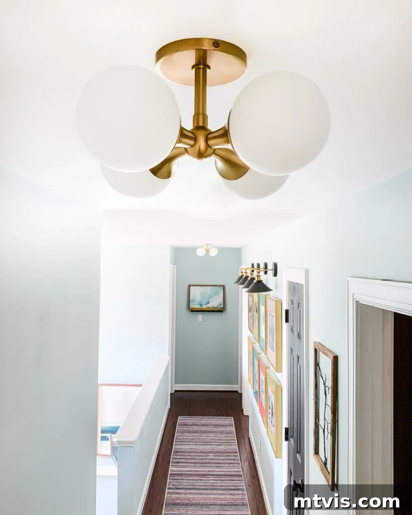 A white light fixture with four round balls hangs from a gold-colored mount on a hallway ceiling.
