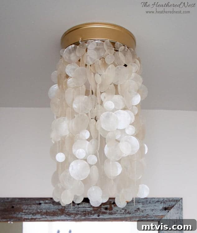 A white Capiz light cover is shown with gold hardware. The light is against a white ceiling.