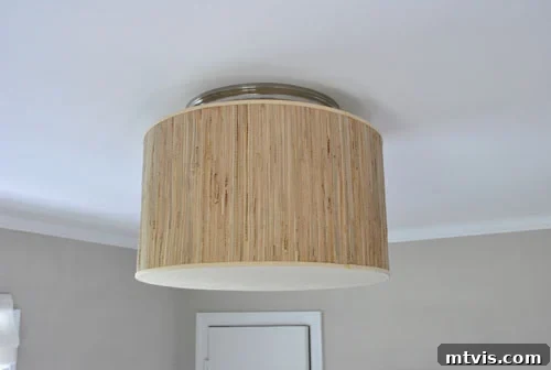A flush mount light is made with a tan lampshade with fabric on the bottom.