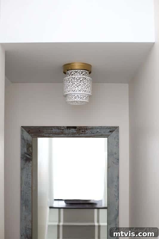 A light fixture is shown in a hallway; the fixture has gold hardware and is made from a white lantern.