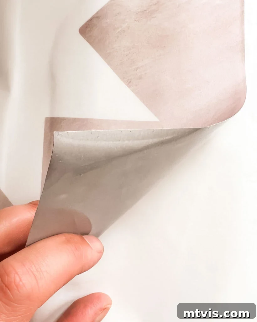 Close-up of a decorative tile sticker being peeled off its paper backing, revealing the adhesive side and vibrant pattern.