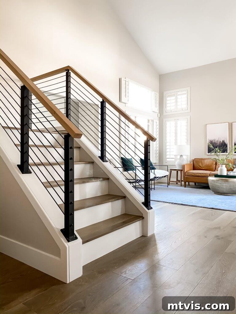 15 Stylish Stair Railing Concepts to Elevate Your Home 4 A metal black cable railing freshens white and wood stairs opening into a living room.