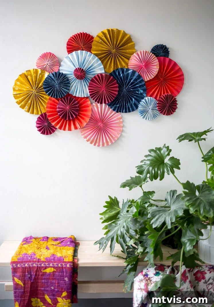 23 Ingenious DIY Wall Art Projects 15 A vibrant display of layered fan art, crafted from bright colored card stock and accented with gold paint, positioned above a bench adorned with a kantha quilt and a lush plant.