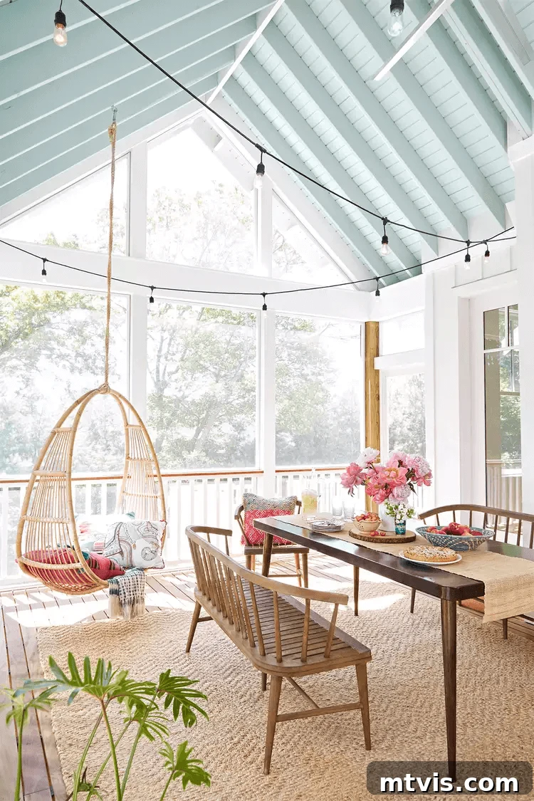 Screened Porch Retreats: Designs for Blissful Outdoor Living 9 Bright and airy screened-in porch idea features a vaulted ceiling painted light blue, string lights, a wooden dining table with bench seating, and a hanging wicker chair with colorful cushions.
