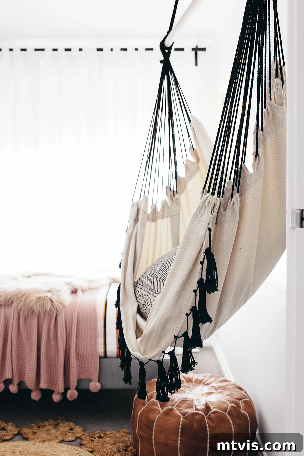 25 Creative Bedroom Transformations for Teenagers 21 A hanging hammock chair in a teen girl's bedroom with a muted pink comforter on the bed and a leather poof underneath.