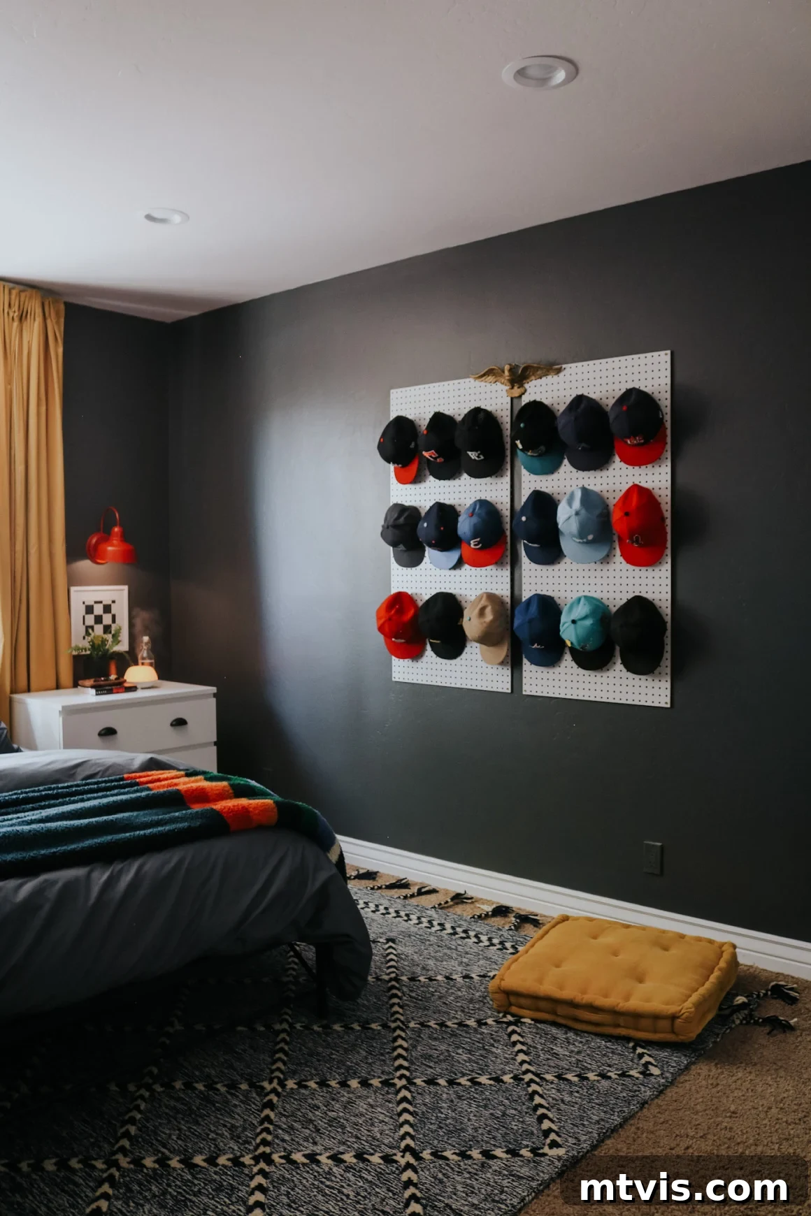 25 Creative Bedroom Transformations for Teenagers 24 Baseballs hats hanging on pegboard as art on a dark wall with a white nightstand in the corner in a teen boy's room.
